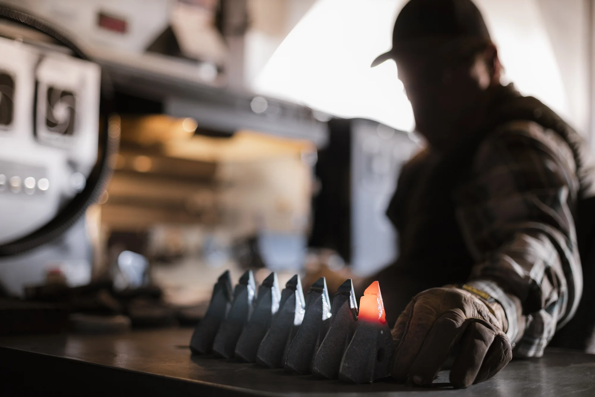 A row of openers on the bench, one tip glowing red hot, with a gloved hand reaching in, at the GEN shop in Coaldale, Alberta