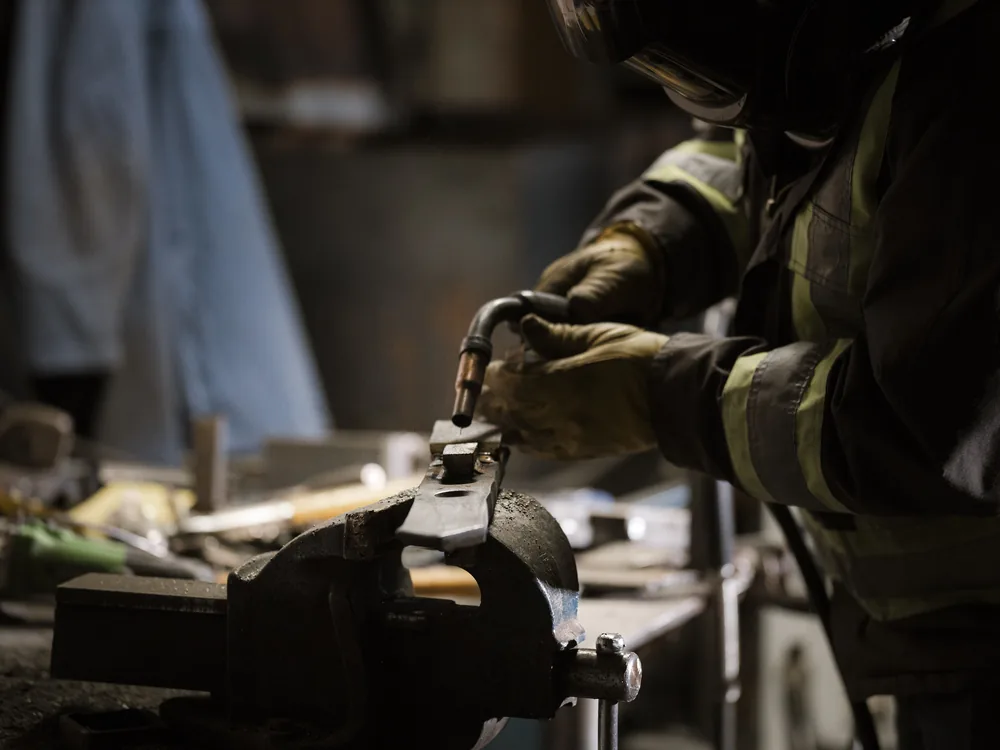 Gloved hands finishing a part held in a vise